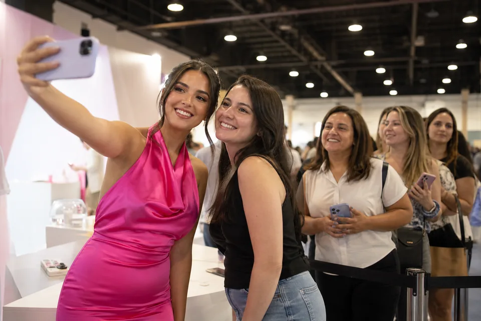 A creator takes a selfie with a fan at a public convention booth while other fans wait in line
