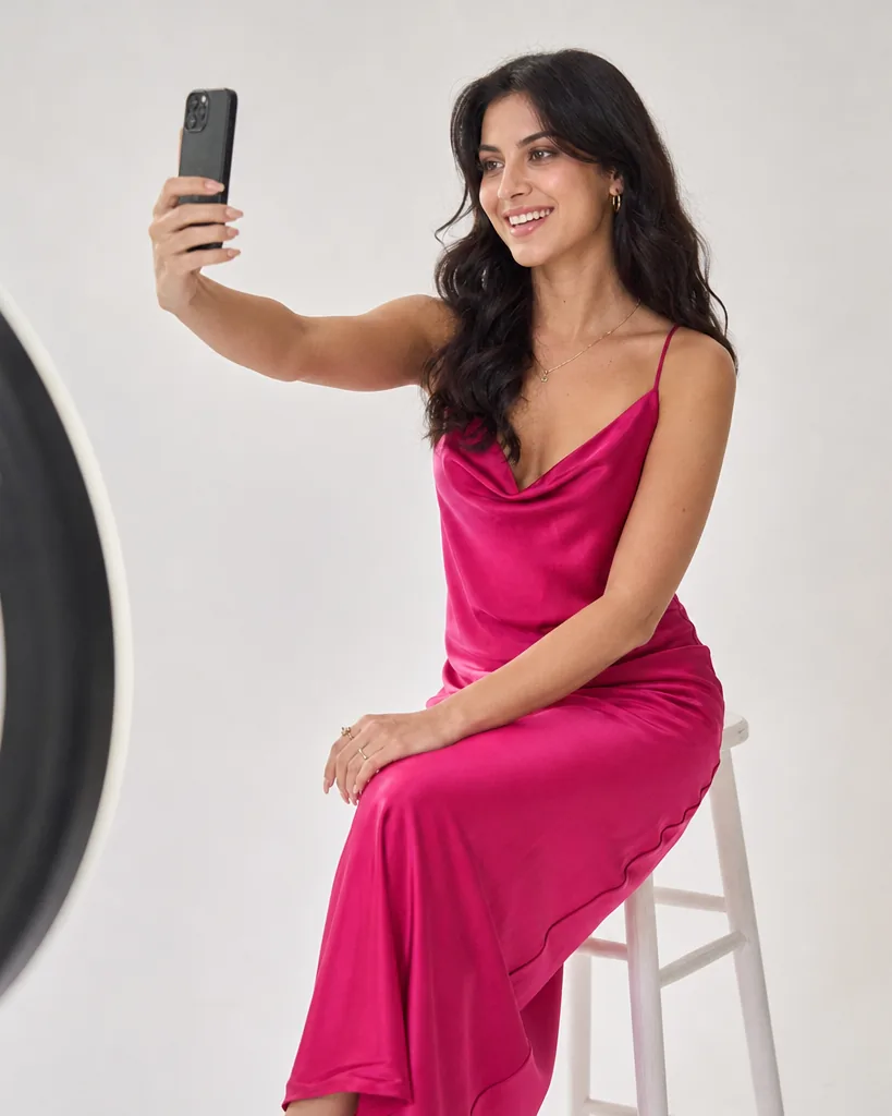 Creator in a fuchsia satin dress holding her phone up for a video call